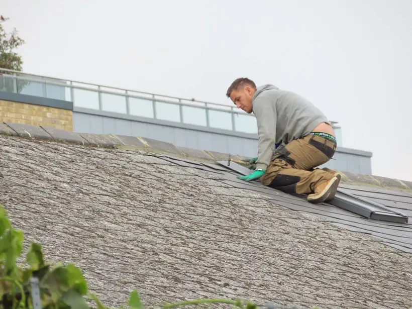 Roofer kneeling on a shingle roof